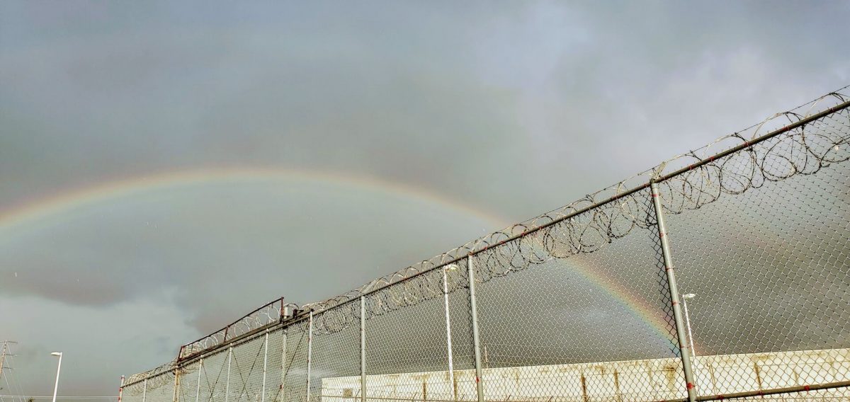 A rainbow arcs above the barbed wire fence of an ICE Detention Center